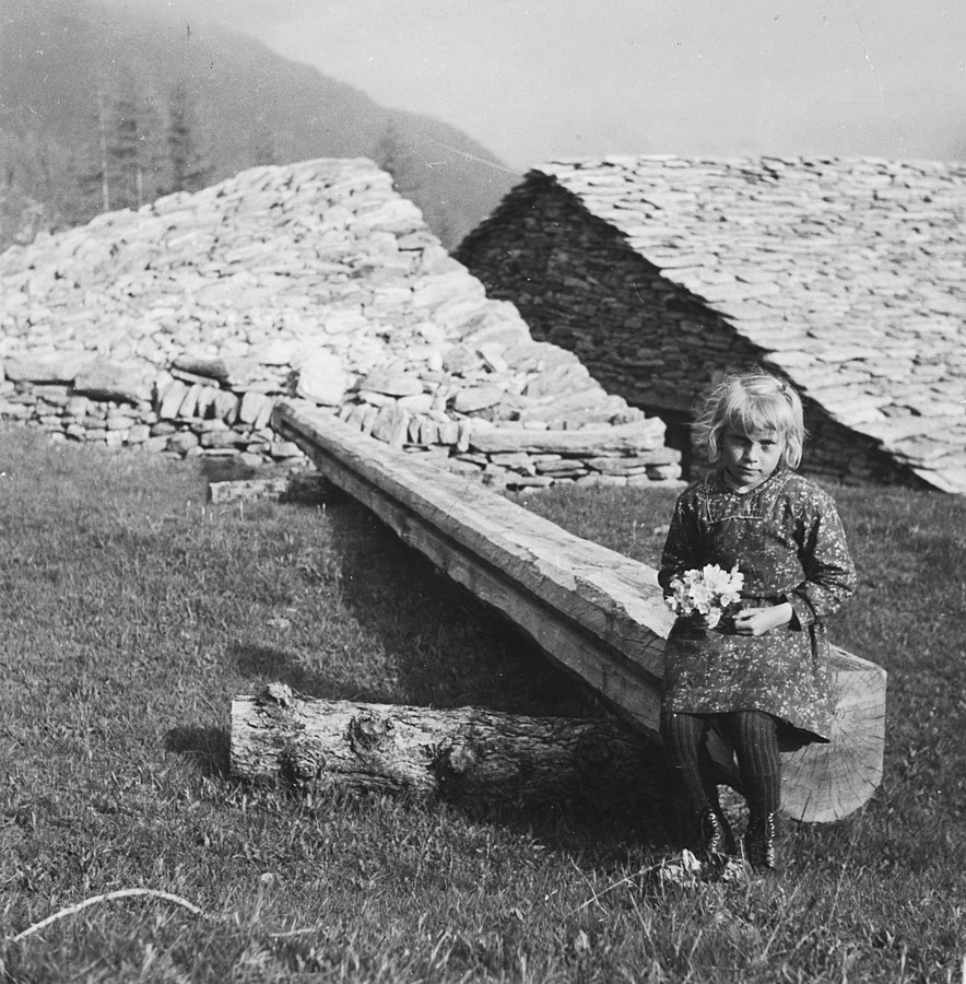 Simplon-Paß: Ein Mädchen mit Blumen in der Hand sitzt auf einem Holzstamm (Foto: Annemarie Schwarzenbach)